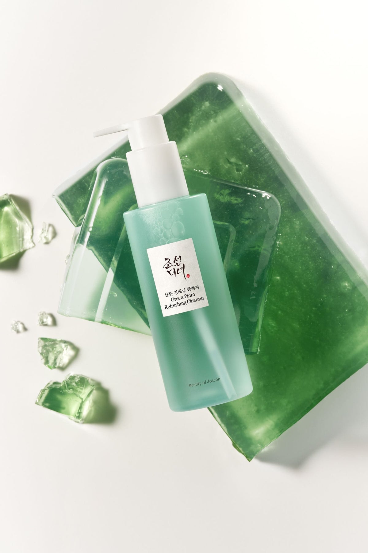 A bottle of Green Plum Refreshing Cleanser with a white pump dispenser, styled on top of translucent green gel pieces against a clean white background.