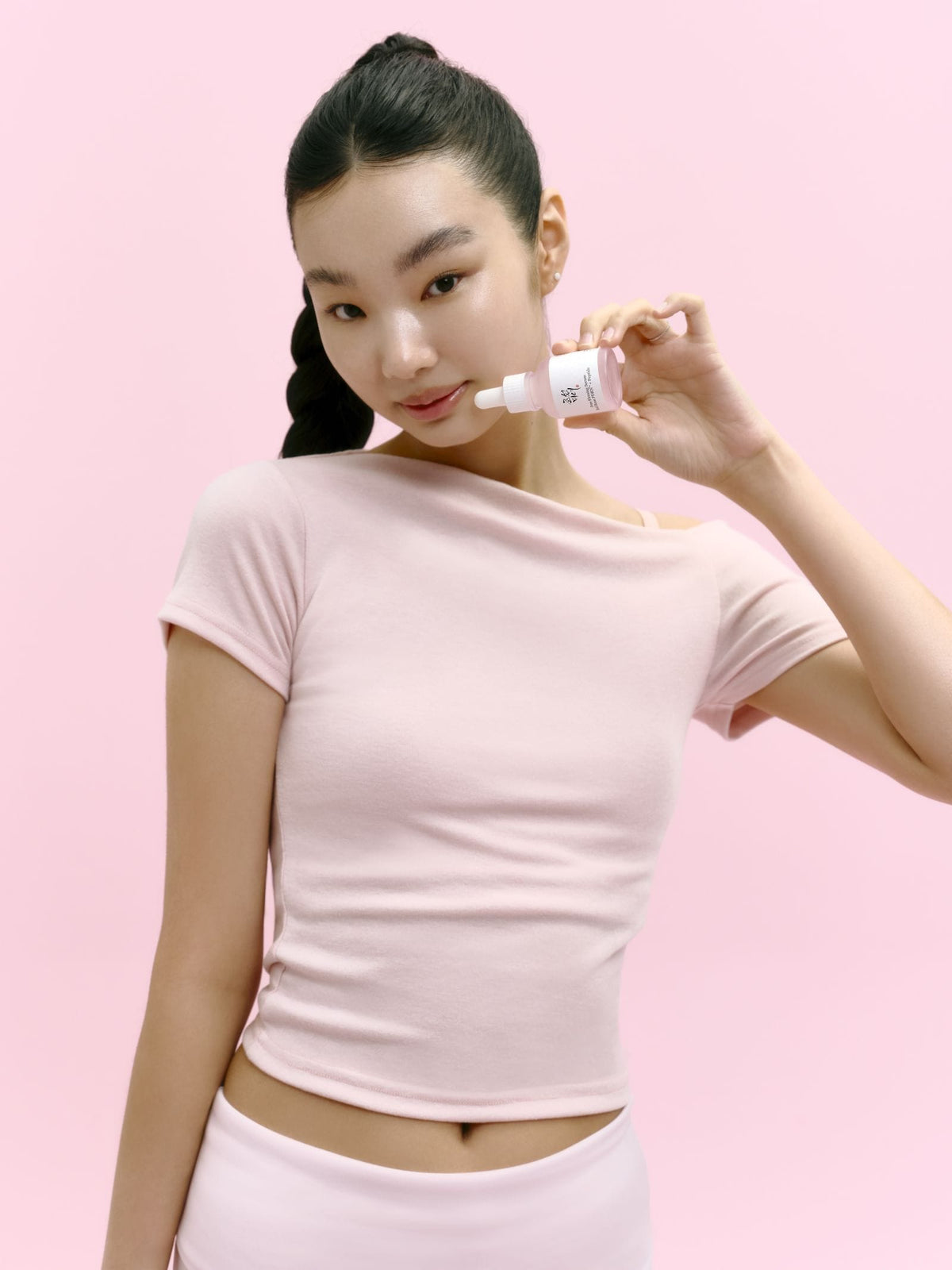 Woman holding a skincare product against a pink background