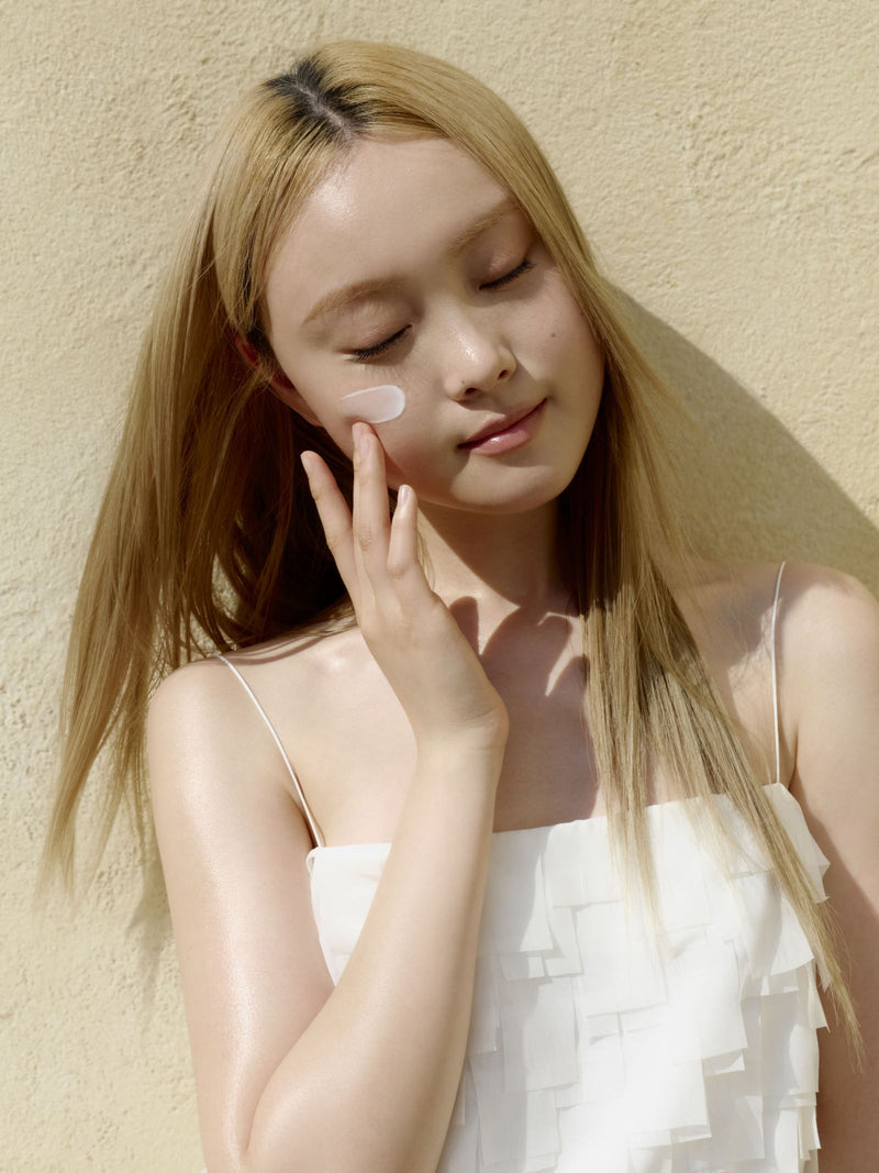 a woman with eyes closed holding a cream on her face