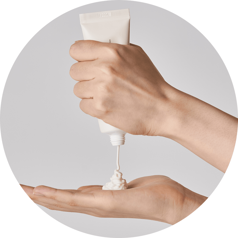 a person's hand pouring cream into a small white object