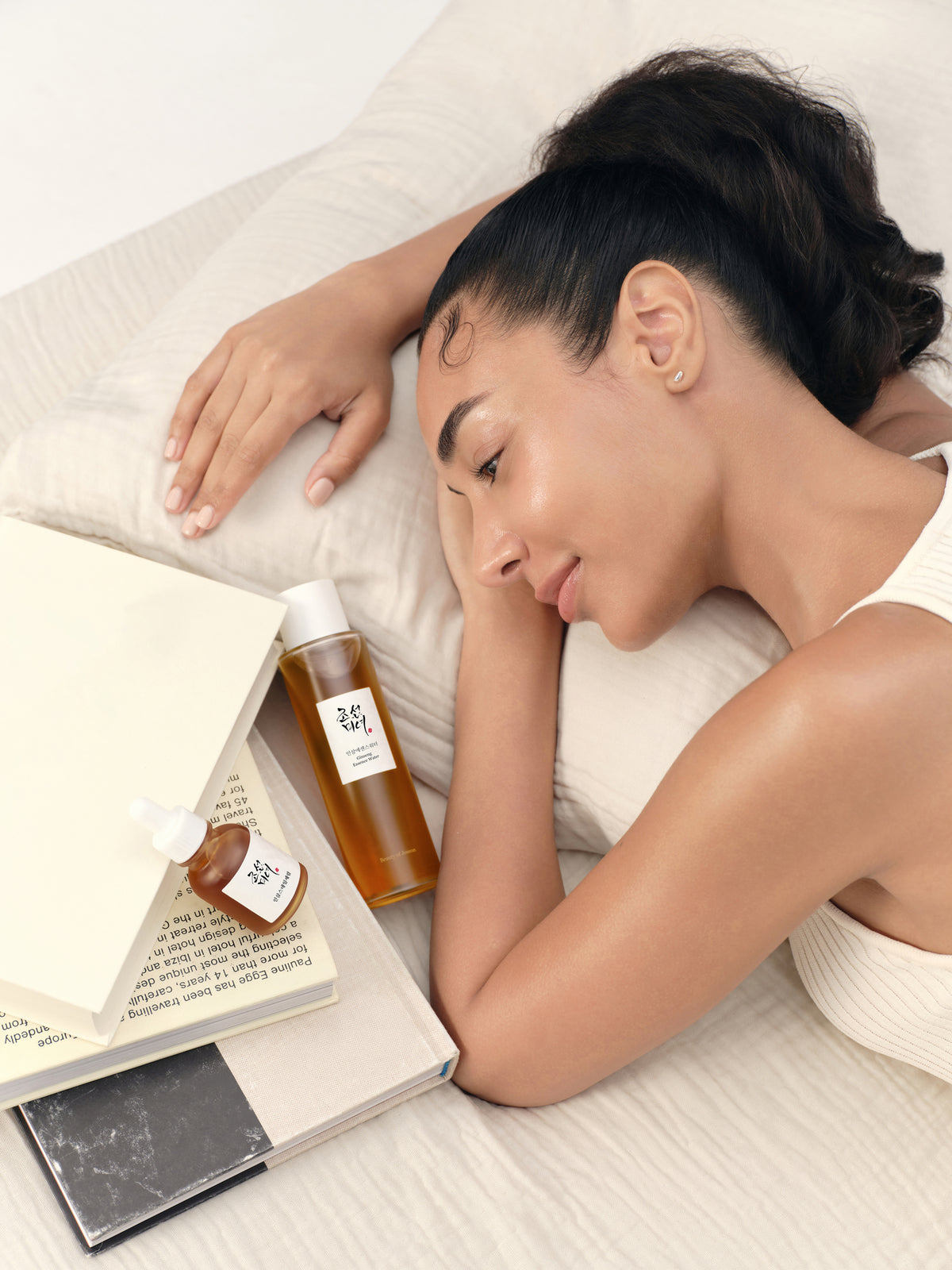 a woman lying on a bed with a book and bottles of oil