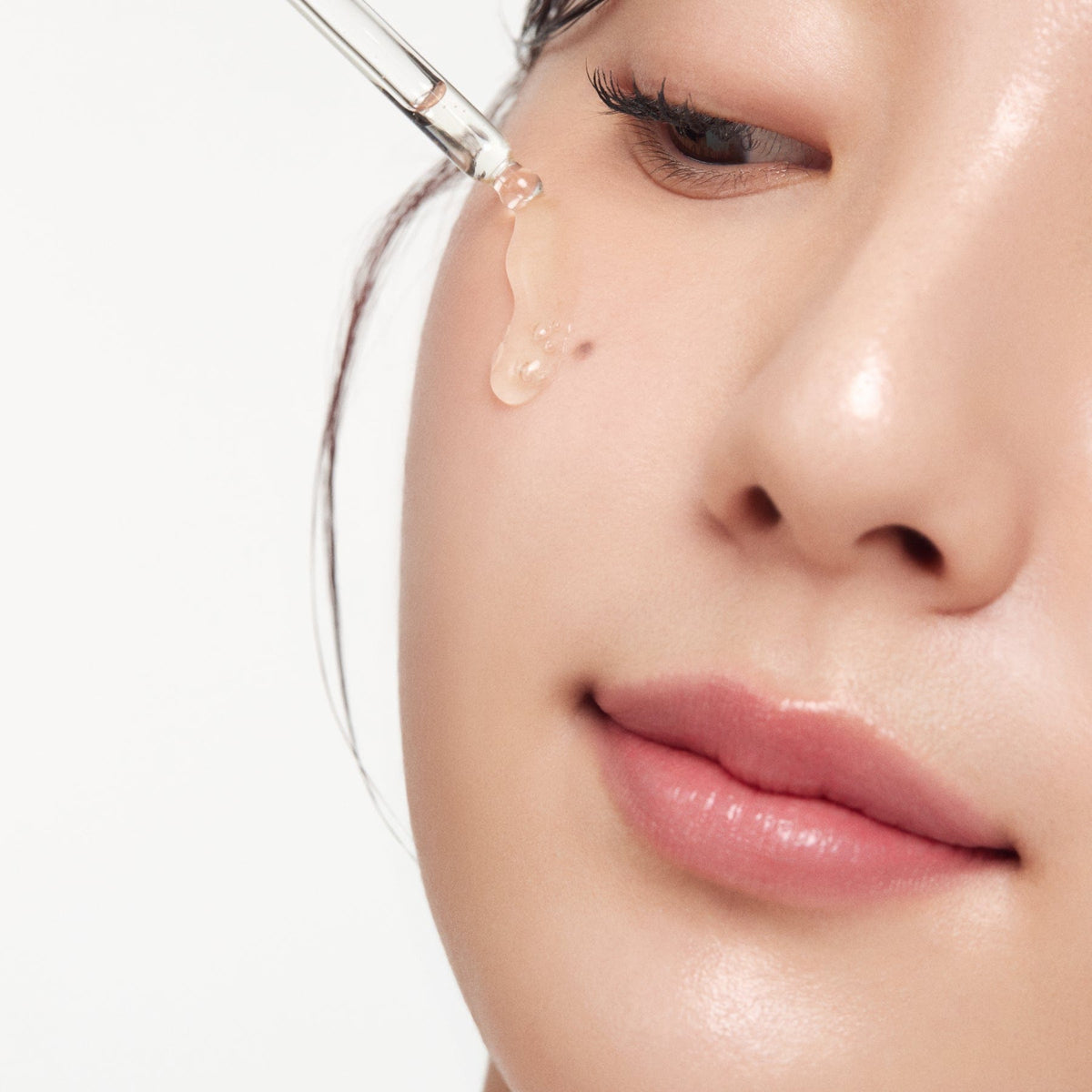 a woman applying a drop of liquid on her face