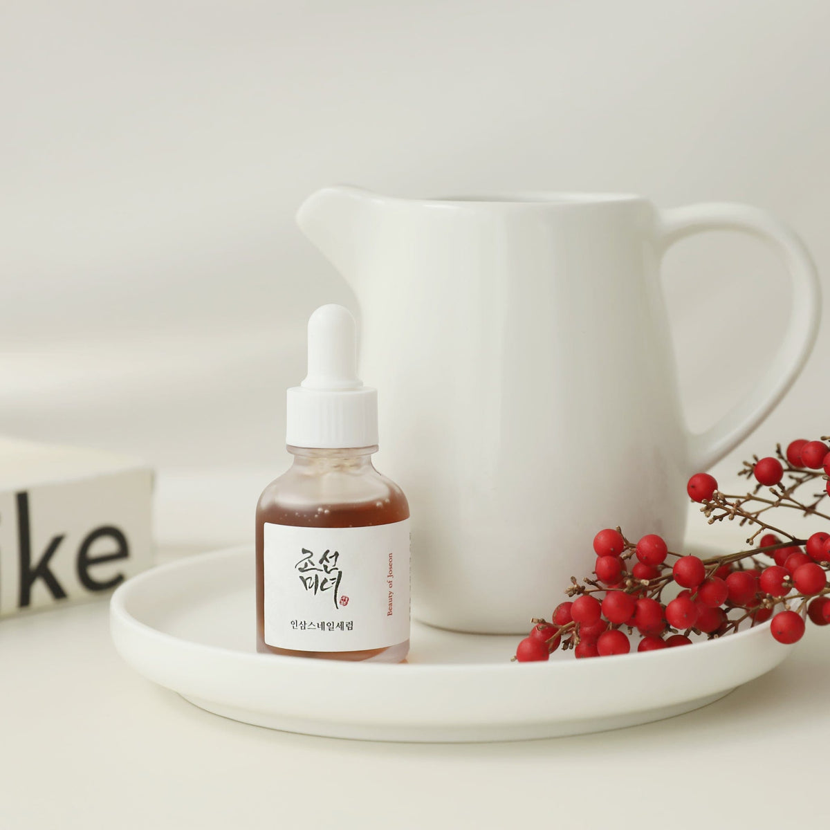 a small bottle of liquid on a plate with a white pitcher and red berries