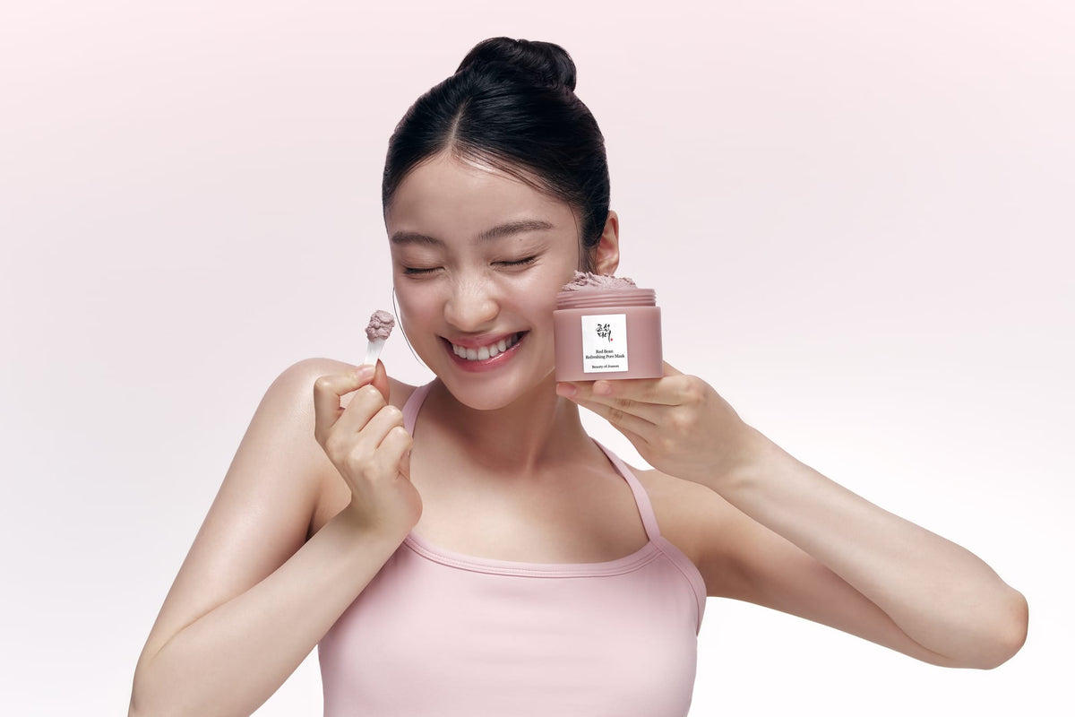 Woman holding a pink skincare product against a light pink background