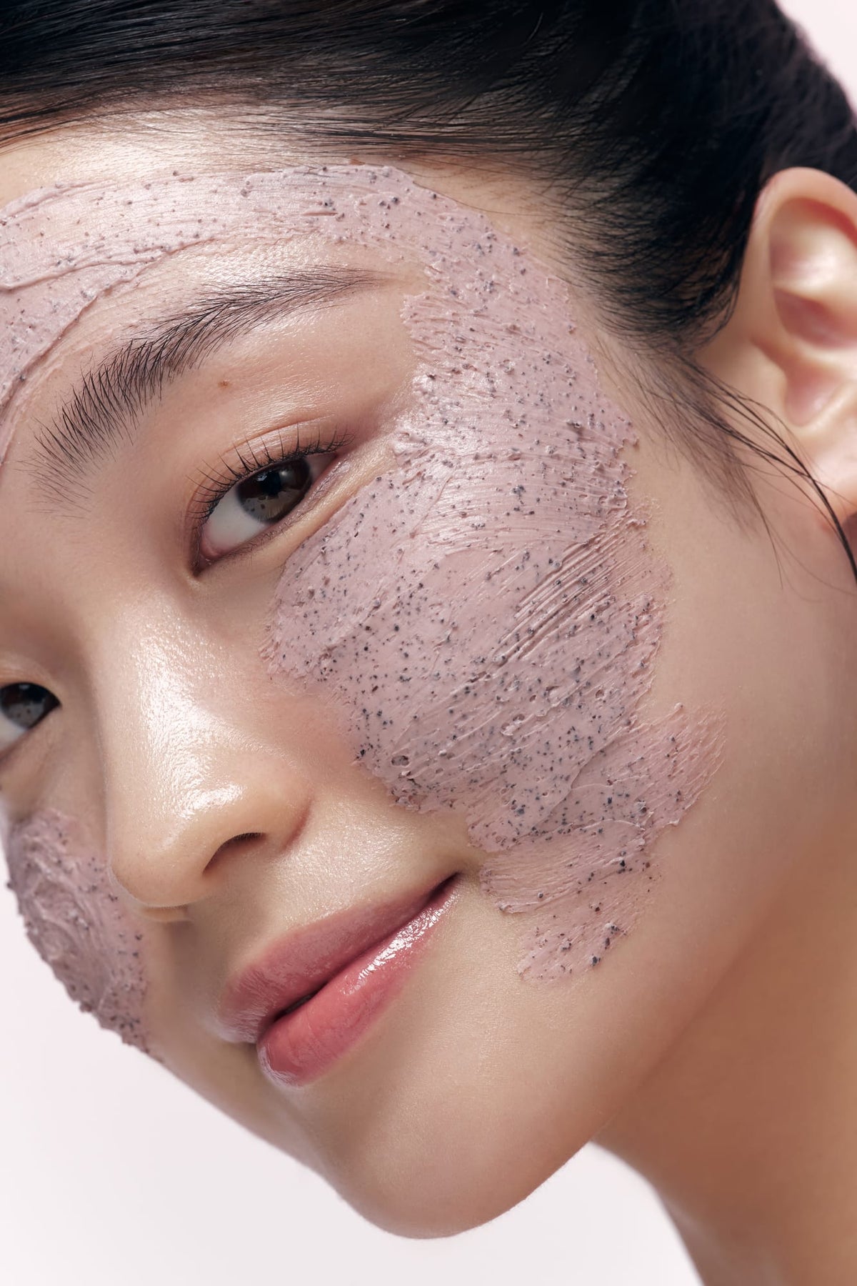 Close-up of a woman's face with a scrub on her skin against a white background